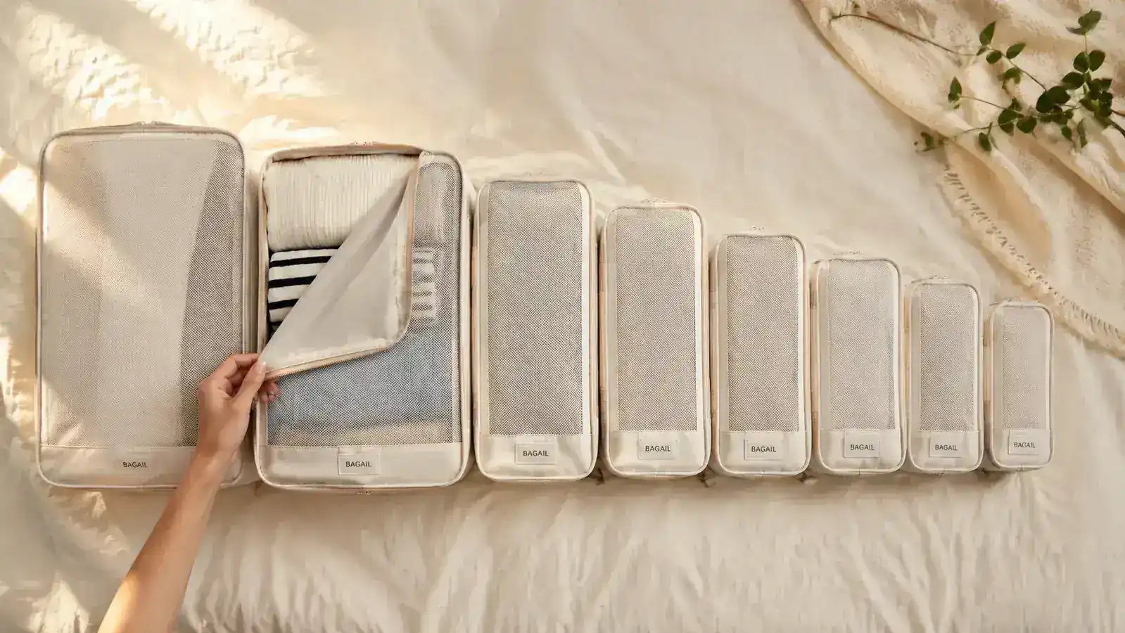 Flat lay of BAGAIL packing cube set showing all 8 sizes sorted by category on a neutral linen surface
