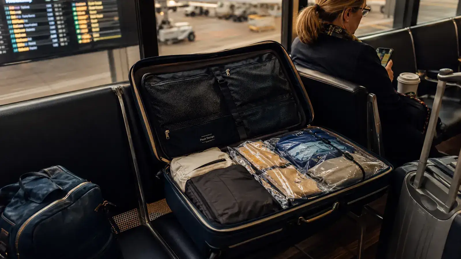 Open carry-on bag at an airport gate with vacuum-compressed bags and packing cubes organized inside
