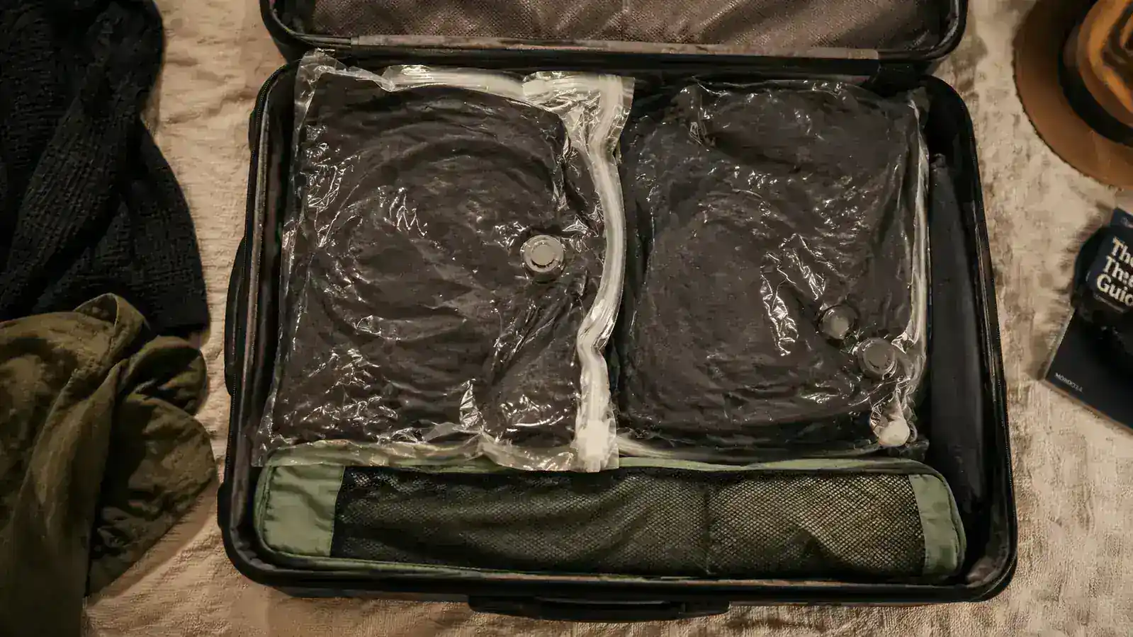 Two vacuum bags packed with dark clothing inside a rolling carry-on suitcase, viewed from above