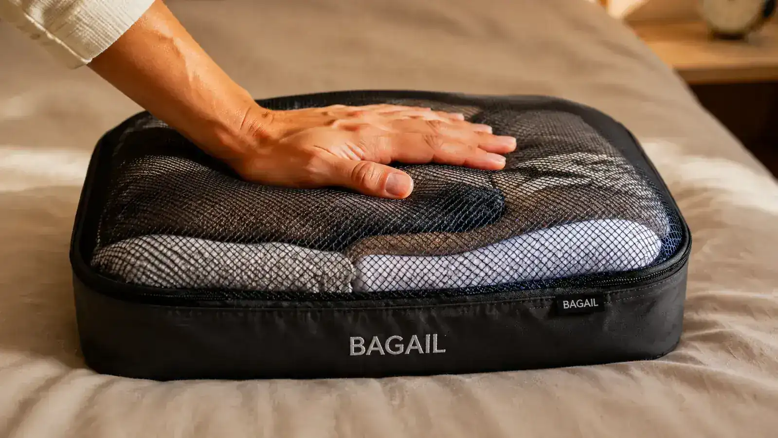 Hand squeezing a mesh packing cube stuffed with rolled t-shirts to demonstrate compression