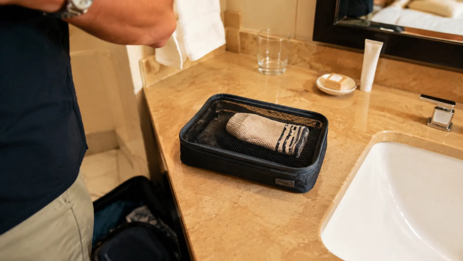 Small laundry packing cube sitting unused next to a hotel sink with a single pair of socks inside