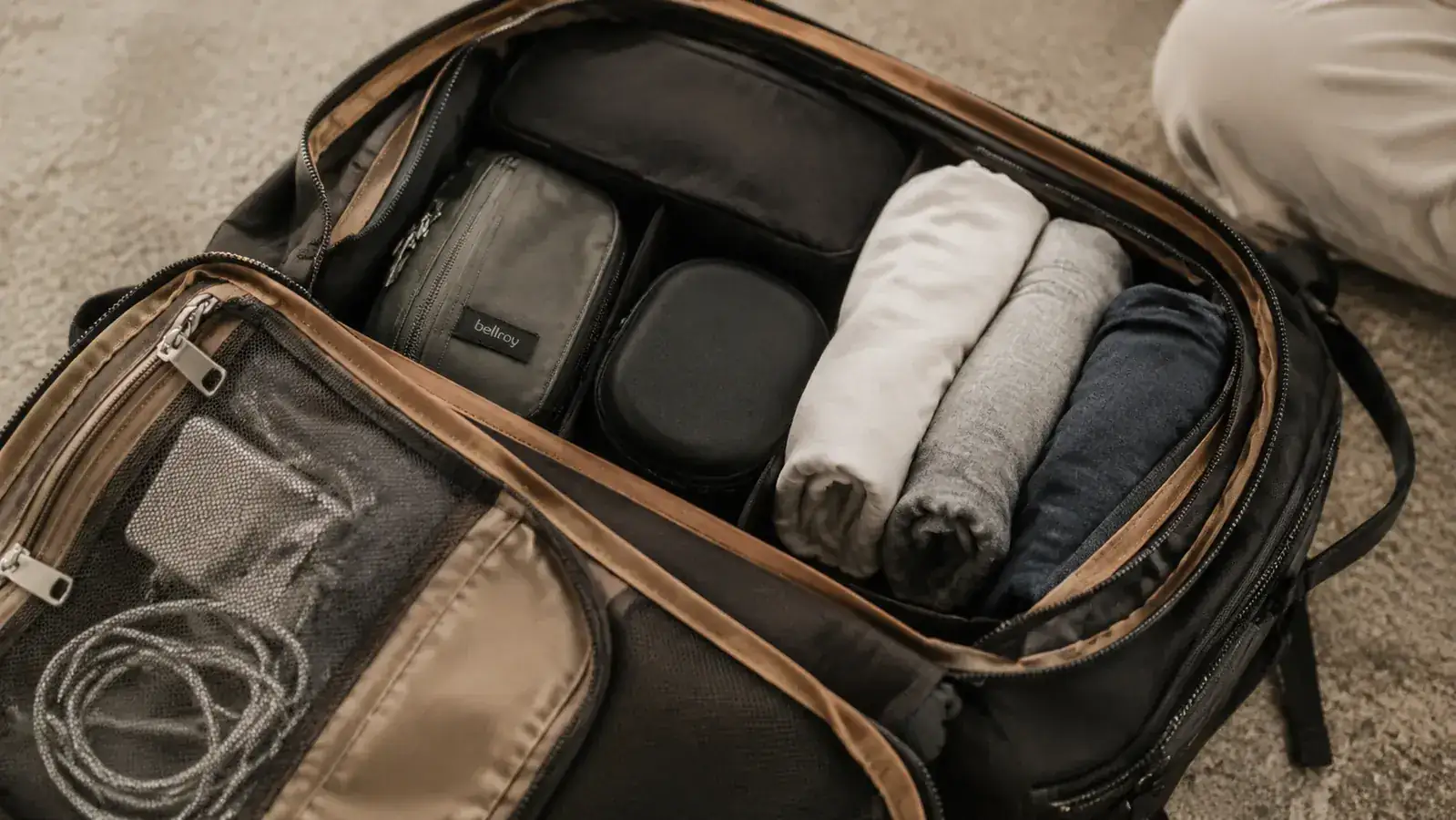Close-up of a coofay backpack's open compartments showing organized packing with a small toiletry bag, rolled clothing, and a phone charger