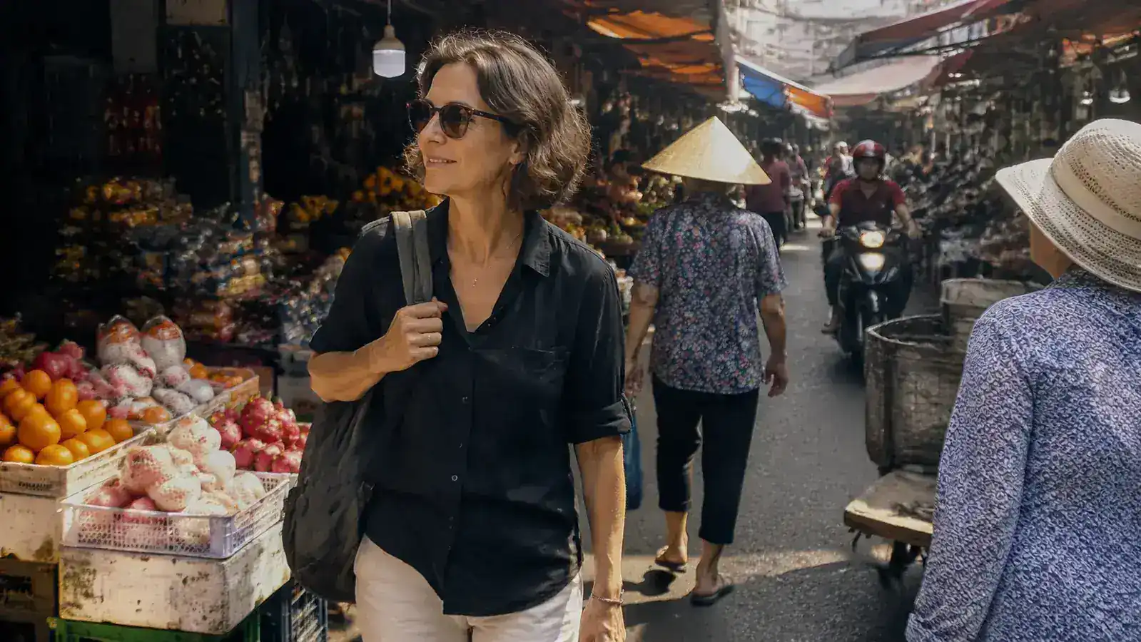 Woman walking through a narrow market alley in Southeast Asia, crowds around her, bag on shoulder, relaxed posture