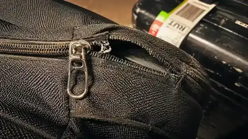 Close-up of a blown zipper on a cheap nylon bag, thread fraying at the pull tab