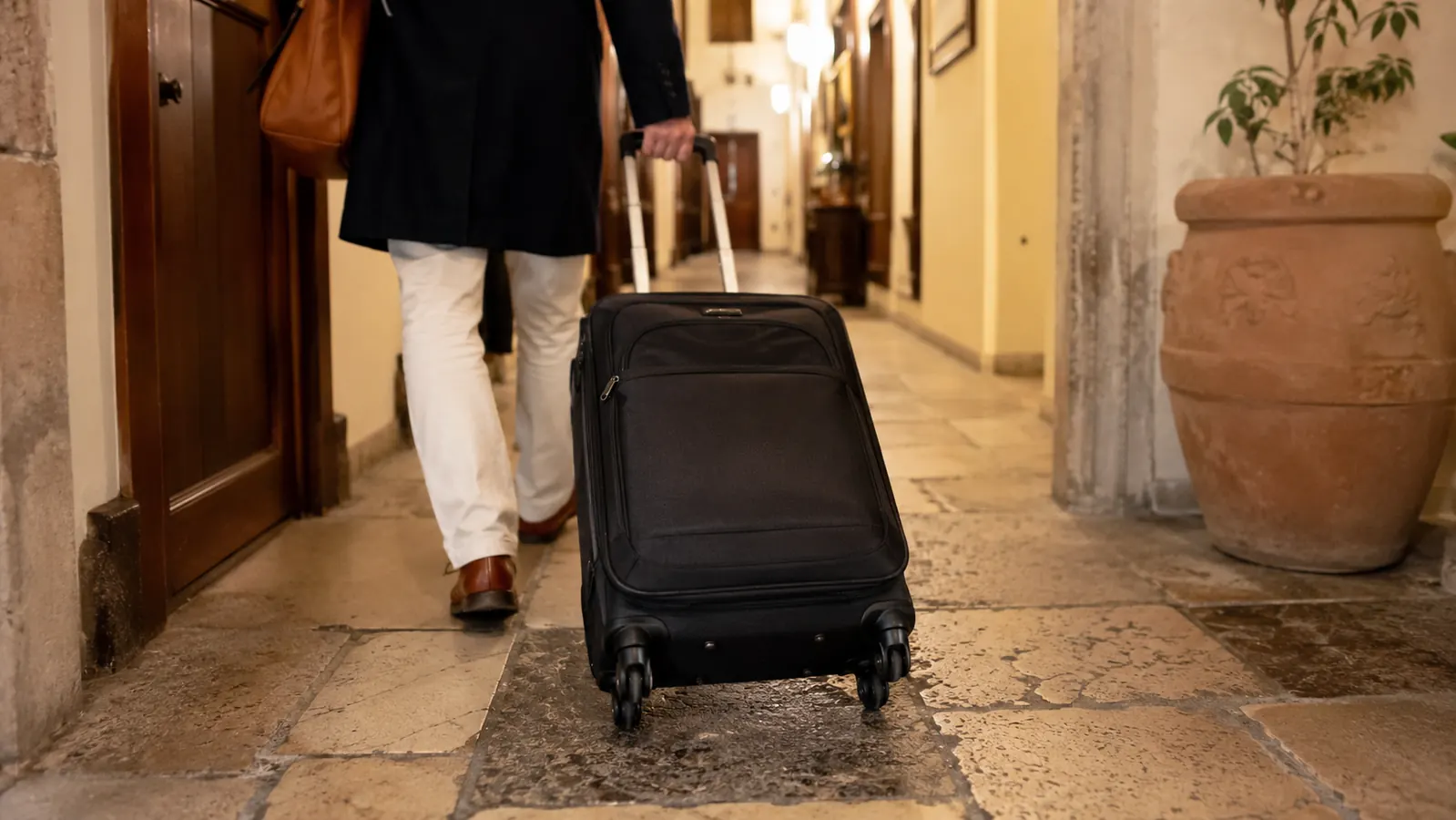 Travelpro Maxlite 5 being wheeled through a narrow hotel corridor, spinner wheels visible from behind