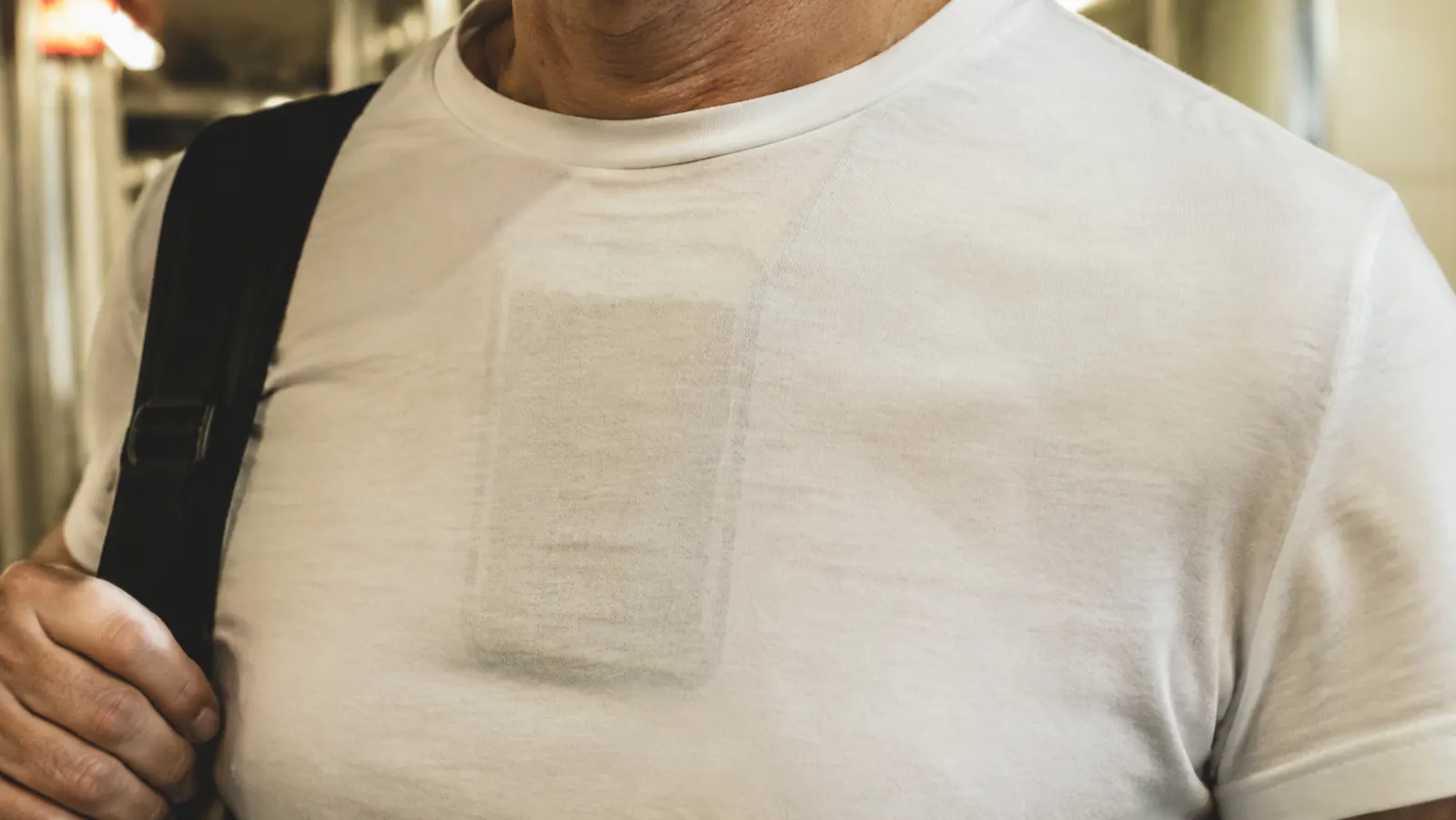 Close-up of neck wallet lump visible under a thin white t-shirt